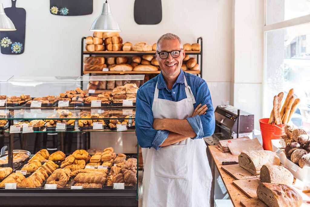 smiling bakery owner in front of store display with breads and pastries