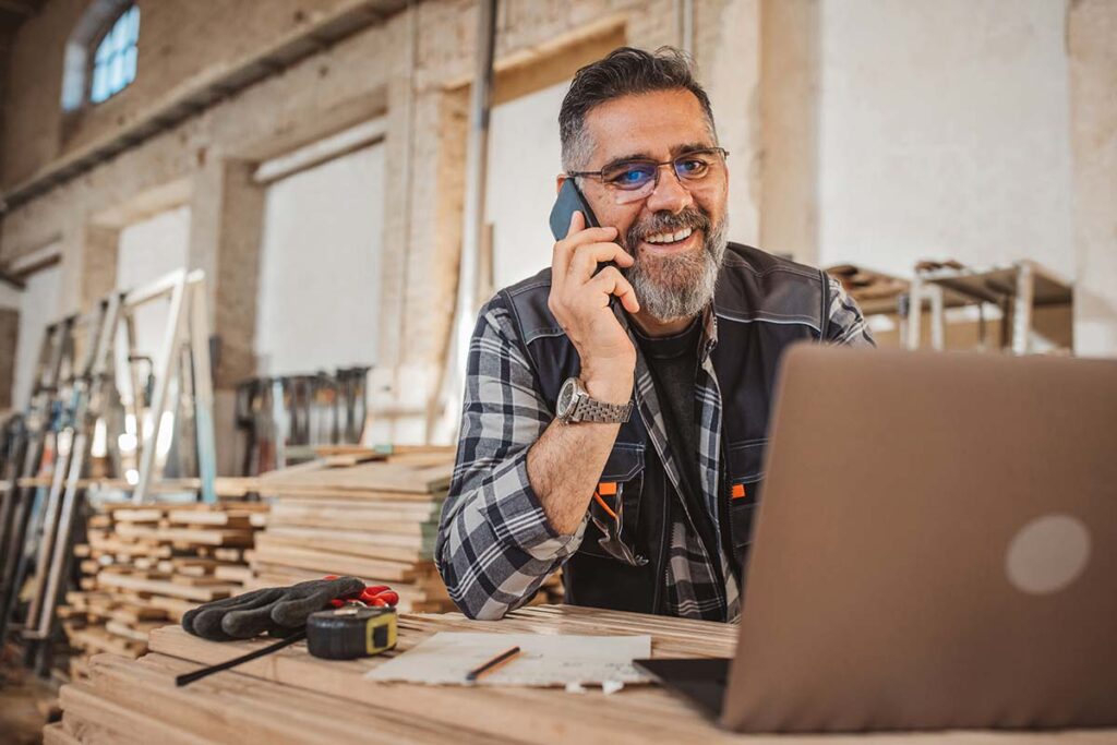 male woodworking business owner smiling on phone in workshop